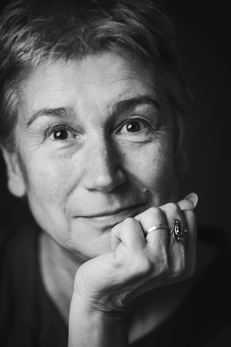 Portrait serré en noir et blanc d'une femme, regard direct, le menton posé sur une main ornée de bagues