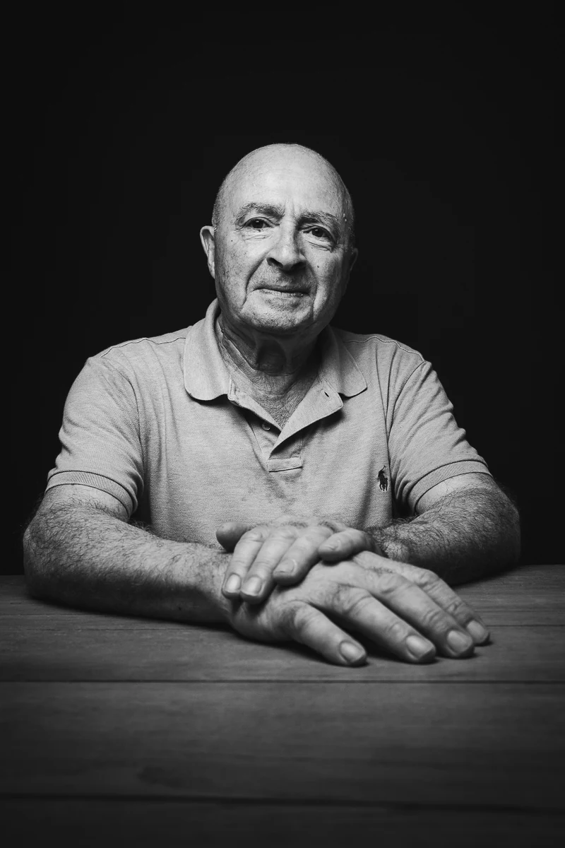 Portrait noir et blanc d'un agriculteur de 65 ans, les mains croisées sur une table en bois, photographié à Montpellier