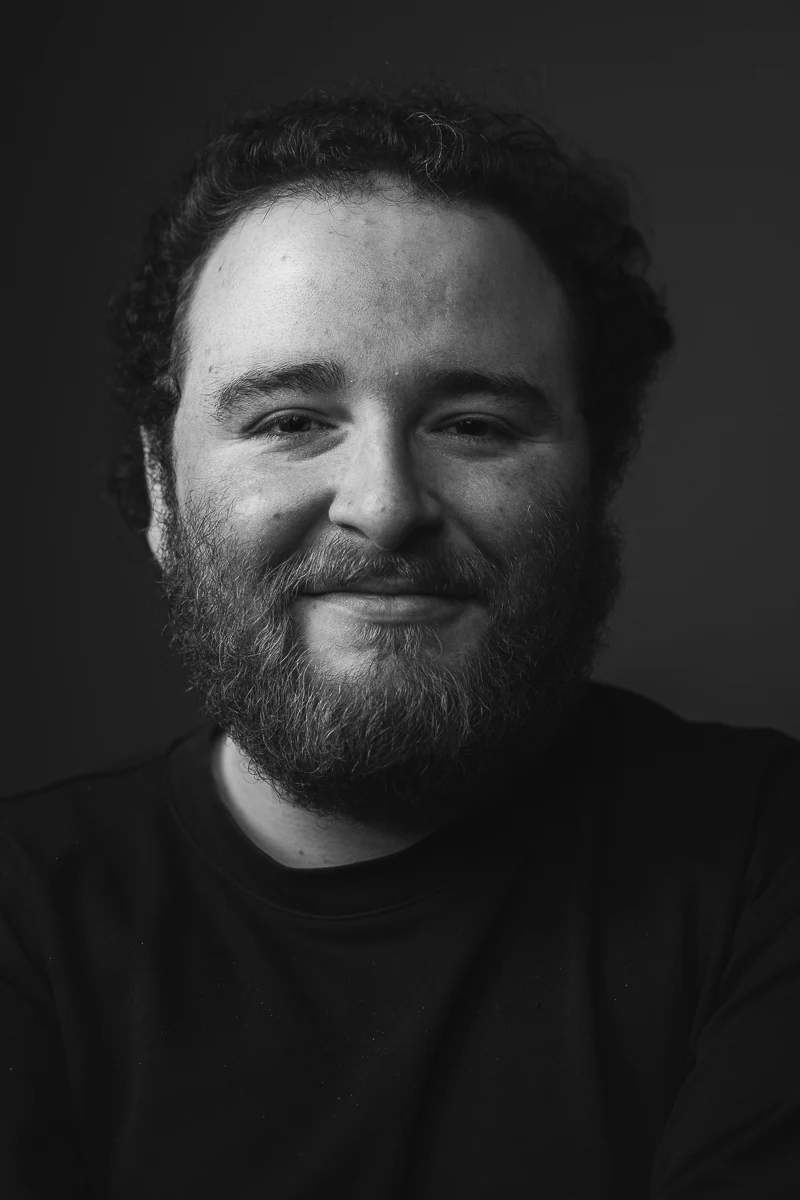 Portrait noir et blanc d'un réalisateur et scénariste aux cheveux bouclés, léger sourire, regard face à l'objectif