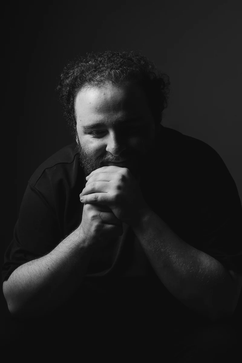 Portrait noir et blanc en clair-obscur d'un réalisateur, les mains jointes devant la bouche